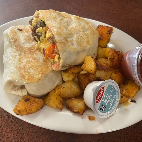 A breakfast burrito with eggs, meat, and vegetables, served with home fries and sour cream.