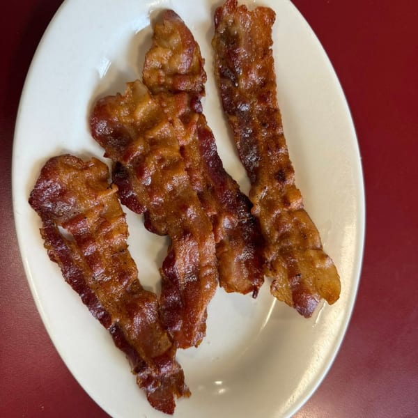 Three strips of crispy, glistening bacon are served on a white oval plate.