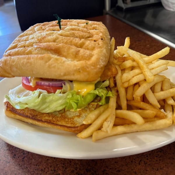 A Dempsey's panini sandwich with lettuce, tomato, onion, and cheese, served with french fries.
