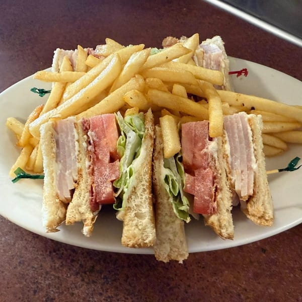 A Dempsey's Breakfast and Lunch club sandwich with ham, lettuce, and mayonnaise, served with golden fries.